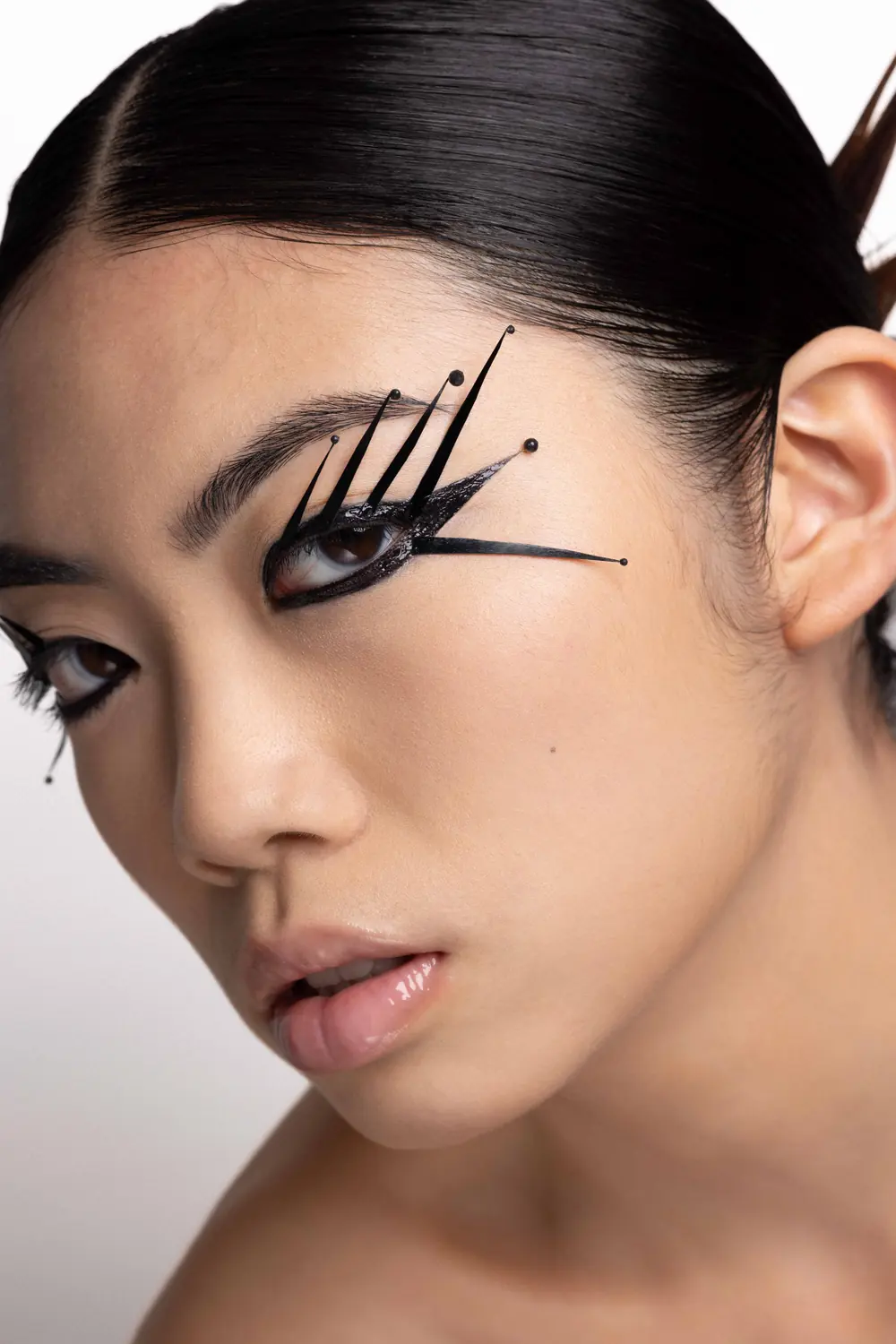 Eye-liner graphique noir en pointes, peau nue et lèvres glossy