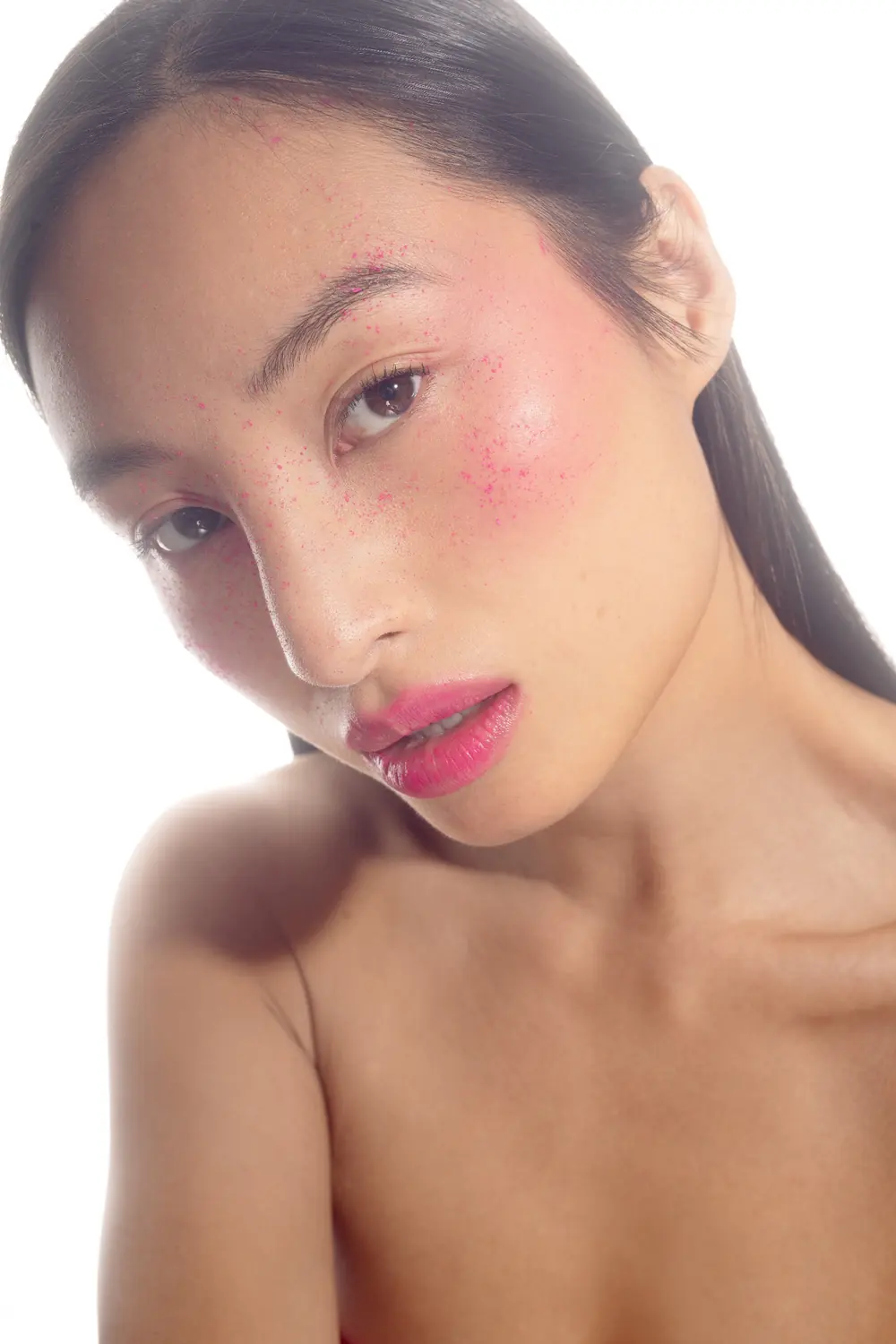 Portrait studio sur fond blanc, peau lumineuse, pigments roses projetés et bouche dégradée