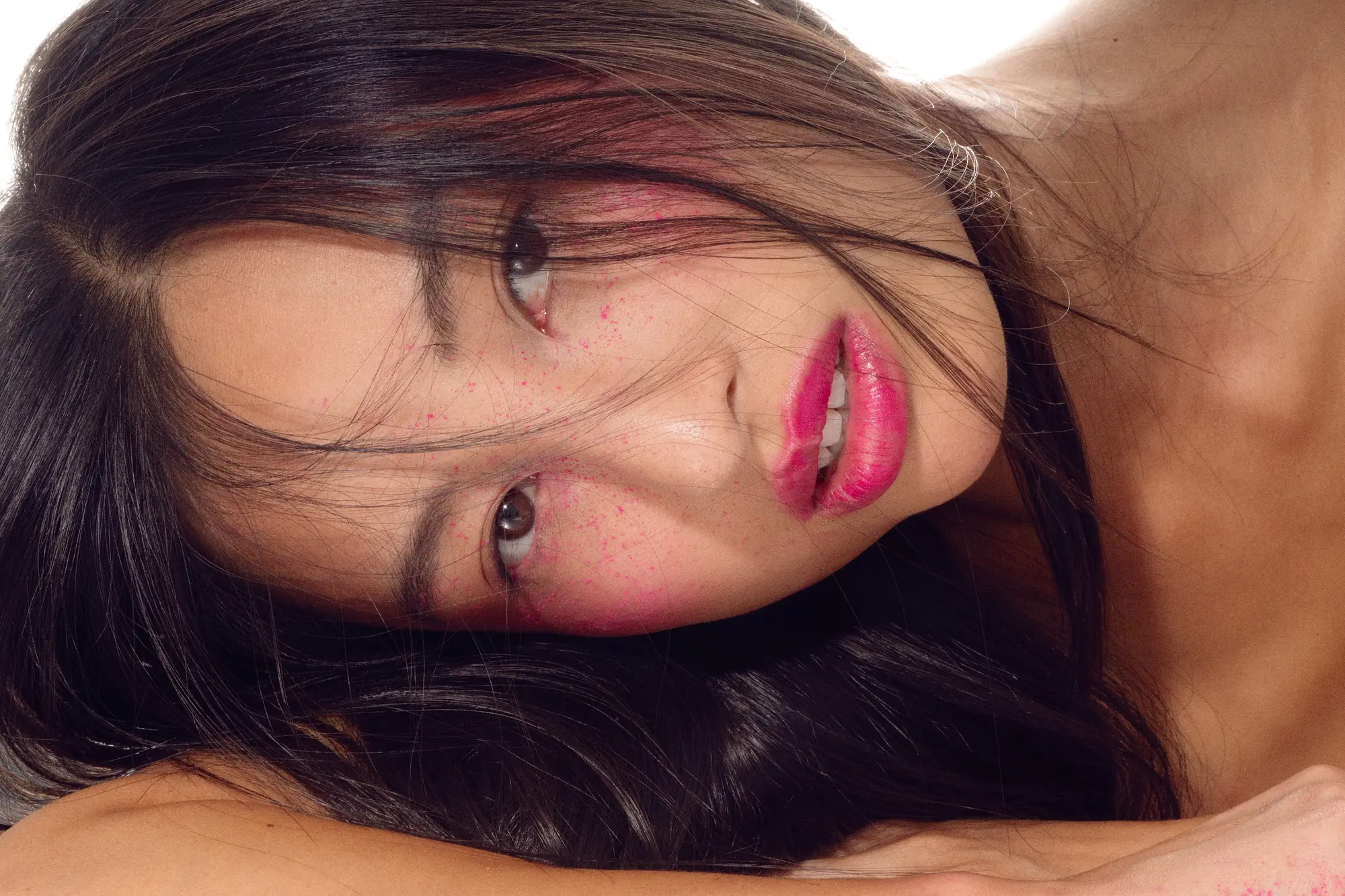 Portrait beauté en studio, tête posée sur le bras, éclats de pigment rose sur la peau et lèvres fuchsia